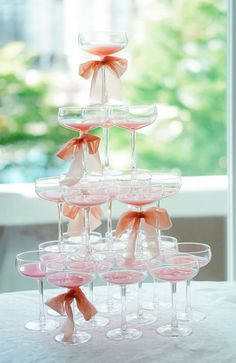 there are many wine glasses stacked on top of each other with pink bows around them