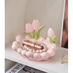 a pink vase with flowers and pearls on it sitting on a shelf next to a magazine