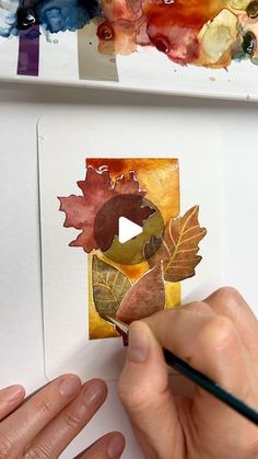 someone is painting leaves on paper with watercolors