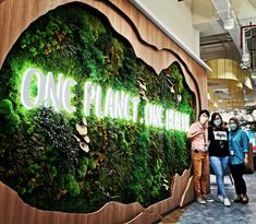 three people standing in front of a green wall with the words one planet on it