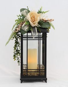 a candle with flowers and greenery in a black lantern holder on a white background