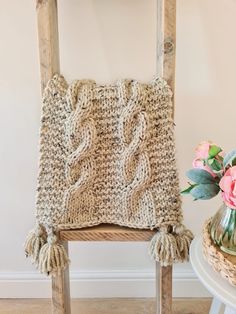 a wooden chair with a knitted cushion on it next to a vase and flowers