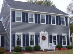 a gray house with blue shutters and wreath on the front door is shown in this image