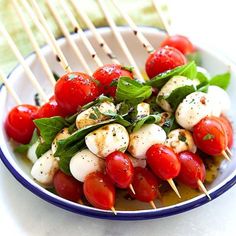 a white bowl filled with tomatoes and mozzarella skewers on top of a table