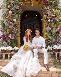 a man and woman sitting next to each other in front of a doorway with flowers