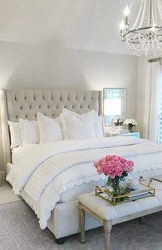 a white bedroom with a chandelier and flowers on the table in front of the bed