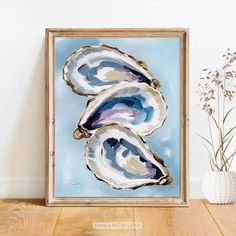 an abstract painting of three oysters on a blue background in a wooden frame next to a vase with flowers