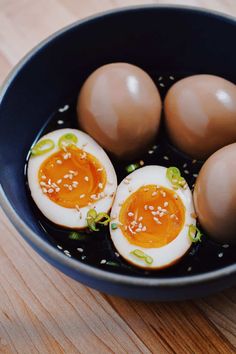 three hard boiled eggs with sesame seeds in a black bowl on a wooden table top