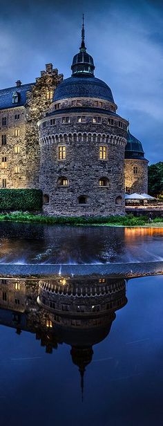 an old castle with a pond in front of it at night, surrounded by greenery