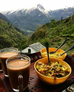 two bowls filled with food sitting on top of a wooden table next to cups and spoons