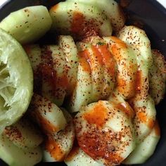 sliced cucumbers in a black bowl with seasoning on the top and green peppers