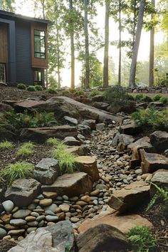 a house in the woods with lots of rocks and grass on the ground next to it