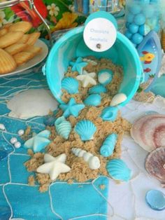 there is a blue bucket filled with sand and seashells on the table next to cookies