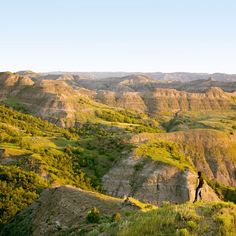 a man standing on top of a lush green hillside next to a valley filled with hills