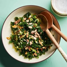 a bowl filled with greens and nuts next to two wooden spoons on a table