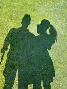 two people standing next to each other on top of a grass covered field with their shadows