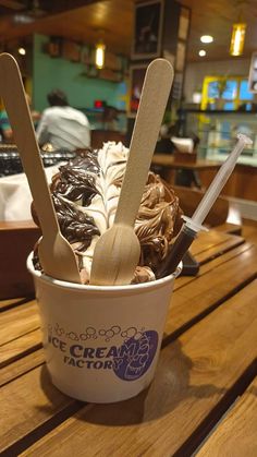 an ice cream sundae with spoons in it sitting on a wooden table at a restaurant