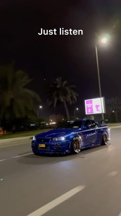 a blue car is driving down the street at night with palm trees in the background