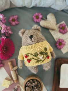 a teddy bear wearing a yellow sweater next to flowers and other items on a table