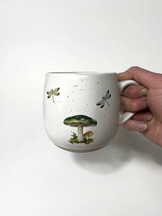 a hand holding a coffee cup with mushrooms and butterflies painted on the outside of it