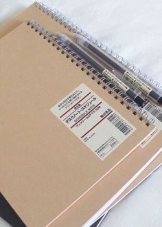 an open spiral notebook with some writing on it and two pens next to the cover