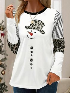 a woman wearing a white and black top with leopard print on the sleeves, standing in front of a christmas tree