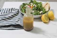 a salad with dressing in a glass bottle next to a bowl of salad and two lemons