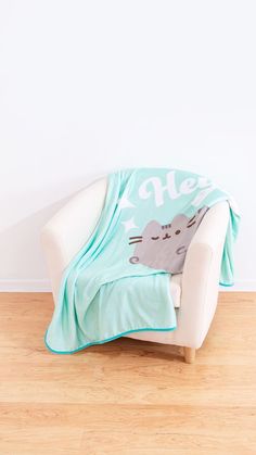 a cat blanket sitting on top of a white chair next to a wooden floor in front of a wall