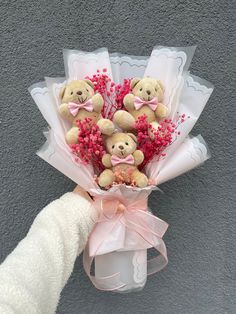 a person holding a bunch of teddy bears with pink flowers in their hand and wrapped in white paper