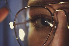 a close up of a woman's eye with glasses on her face and lights in the background