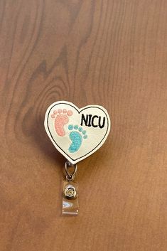 a badge shaped like a heart with the name nicu on it and foot prints