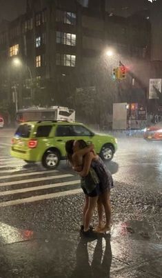 two people kissing in the rain on a city street at night with cars passing by