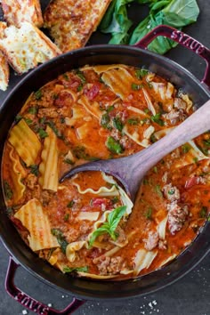 a skillet filled with pasta, meat and sauce on top of a table next to bread