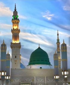 a large white building with a green dome and lights on it's sides at dusk