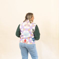 a woman standing in front of a white wall wearing a quilted vest and jeans