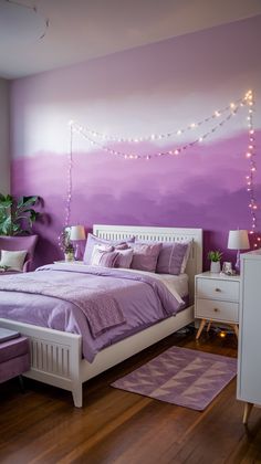 a bedroom decorated in purple and white with string lights on the wall above the bed