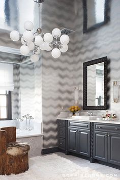 an image of a bathroom with grey cabinets and white marble counter tops, along with a chandelier