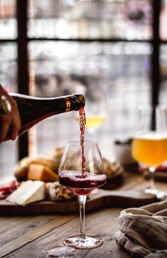 a person pouring wine into a glass on top of a wooden table next to bread