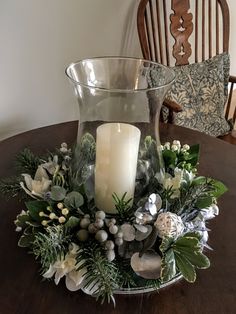 a candle sits on top of a glass bowl filled with greenery and silver ornaments