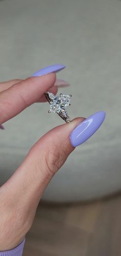 a woman's hand holding a ring with a diamond on it and purple nail polish