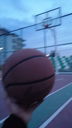 a person holding a basketball up to their face on a court with an overcast sky in the background