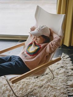 a small child sitting in a rocking chair with a hat on his head and wearing a rainbow shirt