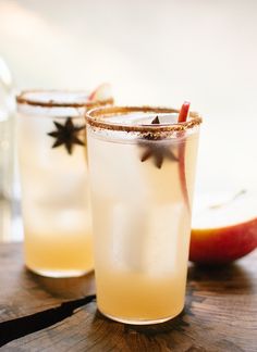 two glasses filled with drinks sitting on top of a wooden table next to an apple