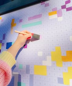 a person holding a knife in front of a wall covered with colored squares and numbers