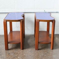 two wooden side tables sitting next to each other on top of a cement floor with a white brick wall behind them