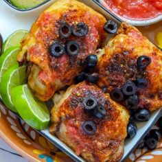 two pieces of chicken with olives and peppers on a plate next to dipping sauce