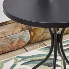 a black table sitting on top of a rug next to a stone wall and floor