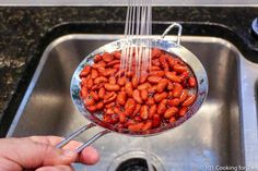 a person is holding a strainer full of hotdogs in the kitchen sink