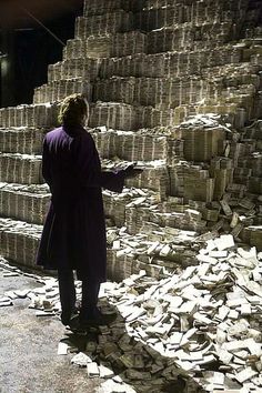 a man in a purple coat standing next to stacks of cement bricks and looking at something on the ground