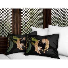 two black and gold pillows on a white bed with bamboo screens in the back ground